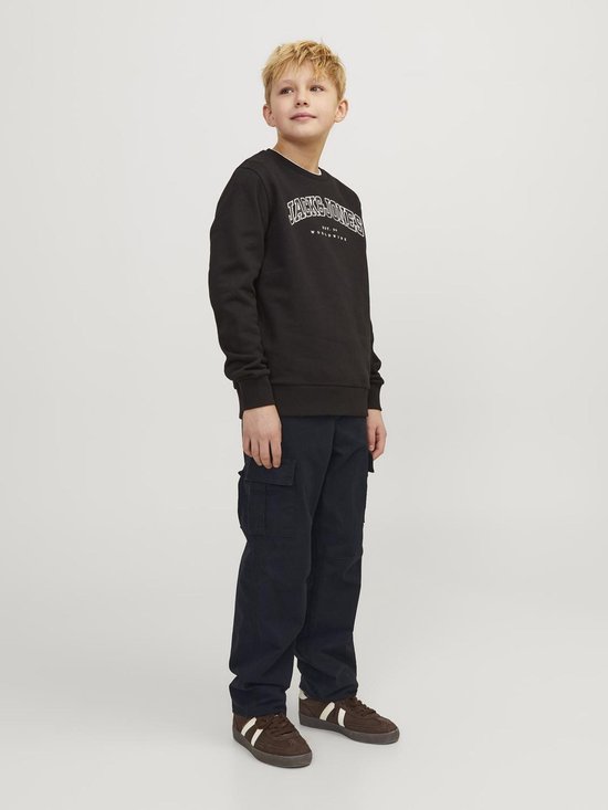 Jongens in een zwarte trui met logo en donkere cargobroek, met bruine sneakers met witte strepen.