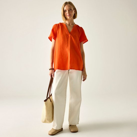 Model draagt een oranje blouse met korte mouwen en een V-hals, gecombineerd met een witte broek.