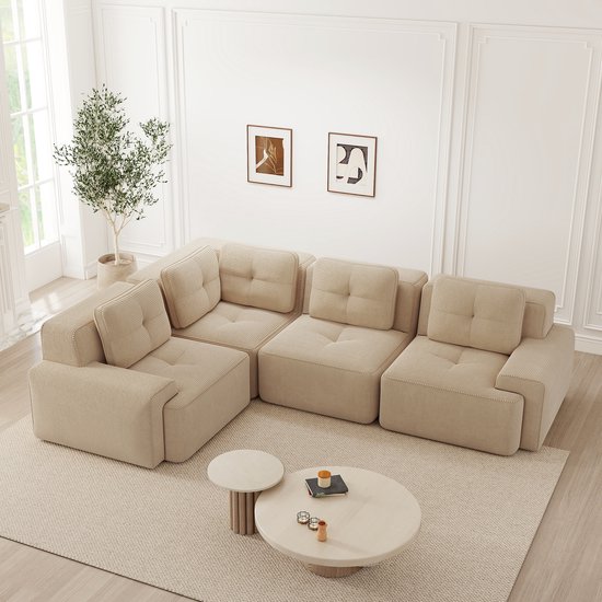 Beige corduroy hoekbank met diepe zitplaatsen, bestaande uit meerdere modules, met vierkante kussens.