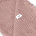 Detail van lichtroze mousseline stof met franjes en een Lionelo label.