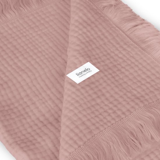 Detail van lichtroze mousseline stof met franjes en een Lionelo label.