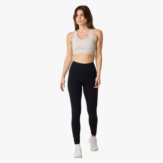 Model van voren gezien, draagt een lichte sportbeha met racerback en zwarte legging met logo. Ze loopt naar voren.