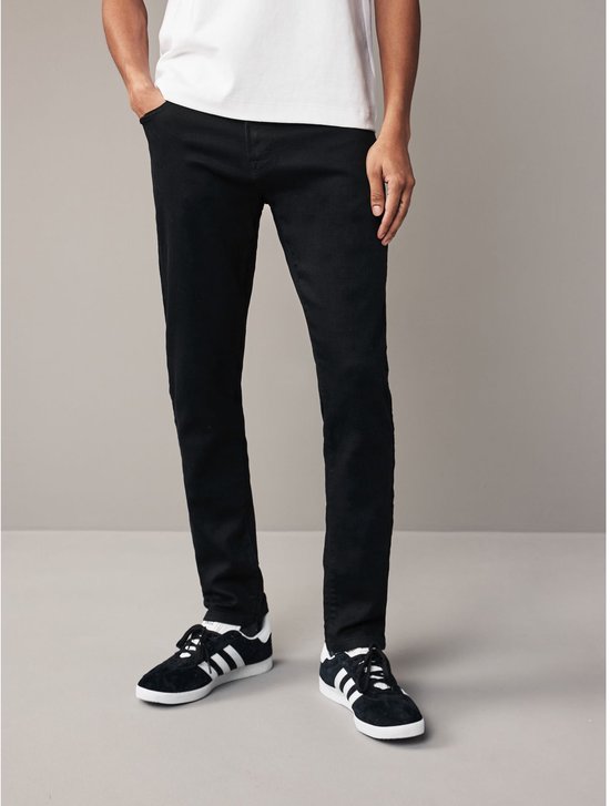 Man in zwarte skinny jeans en zwarte sneakers met witte strepen.
