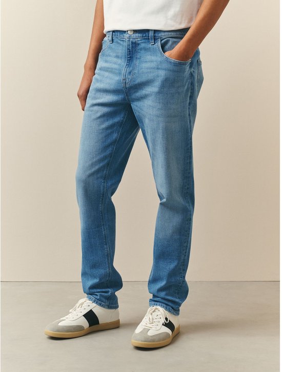 Man in een lichte wassing skinny fit spijkerbroek met een witte T-shirt en sneakers.