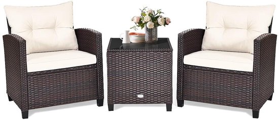 Donkerbruine rotan fauteuils met crèmekleurige kussens, met een bijpassend tafeltje met glazen blad en een vaas met bloemen.