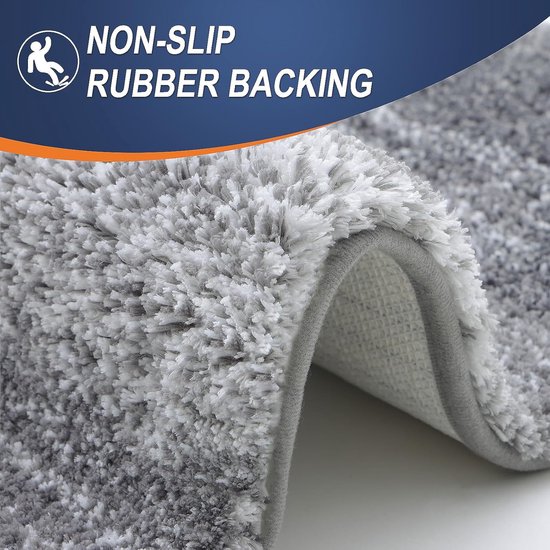 Close-up van een zacht grijze badmat met de tekst 'NON-SLIP RUBBER BACKING'.