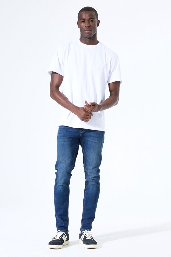 Model draagt een witte T-shirt en een donkerblauwe slim fit jeans met donkere sneakers.