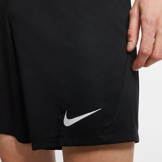 Homme portant un short de sport Nike noir avec un logo Nike blanc sur la jambe gauche. Il porte des chaussettes blanches et des chaussures de football.