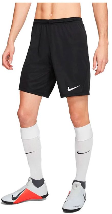 Homme portant un short de sport Nike noir avec un logo Nike blanc sur la jambe gauche, des chaussettes blanches et des chaussures de football.
