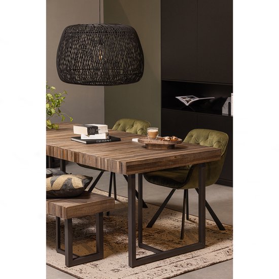 Eettafel van hout met metalen onderstel, omringd door groene fluwelen stoelen en een zwarte bank. Een grote zwarte hanglamp hangt erboven.