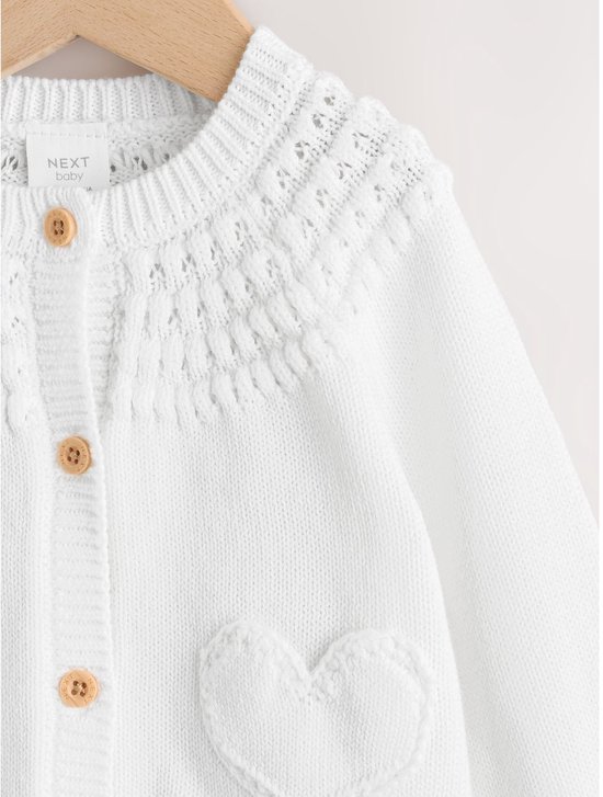 Witte babyvest met gebreide hartjes op de zakken, ajourdetails en houten knopen.