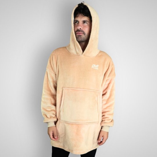 Een man met krullend bruin haar draagt een beige hoodie deken met de capuchon omhoog. Hij kijkt naar de zijkant.