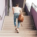 Man met een bruine leren rugzak op zijn rug, lopend op een trap.