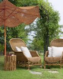 Bruine kokos parasol met golvende randen naast rieten stoelen in een tuin, met een bijzettafel en beplanting.