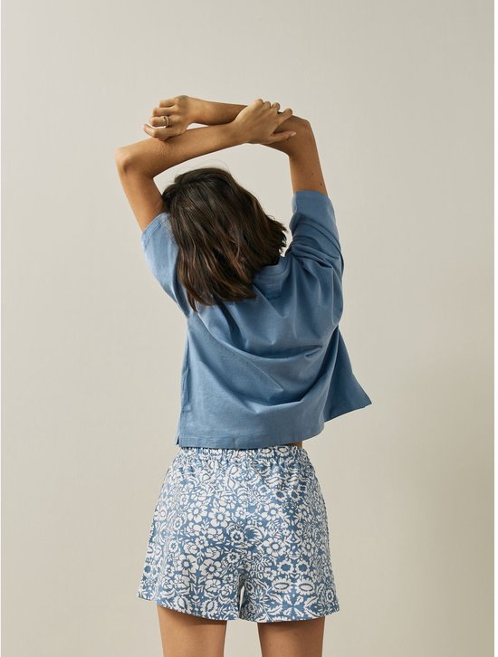 Model met rug naar ons toe, draagt blauw shirt en korte pyjamabroek met bloemenprint.
