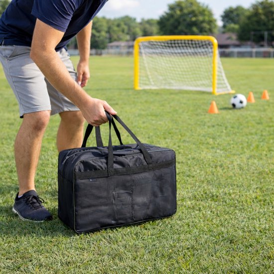 Man met een zwarte sporttas op een voetbalveld.