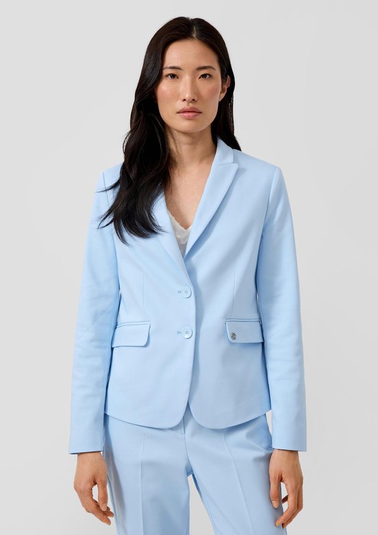 Vrouw in lichtblauwe blazer en broek, witte kanten top zichtbaar.