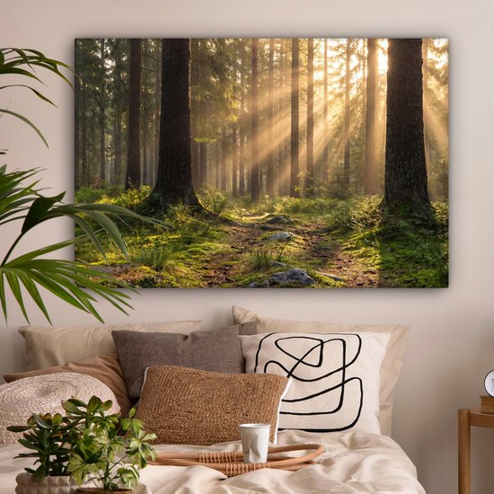 Een slaapkamer met een groot canvas schilderij van een bos met zonlicht op een pad. Naast het bed staan kussens en een plant.