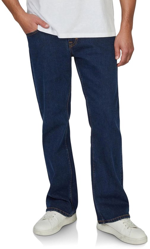 Voorkant van een man in donkerblauwe bootcut jeans met oranje stiksels en witte sneakers.