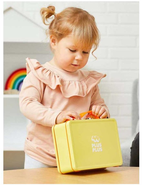 Een jong kind in een roze trui met ruches sluit een gele Plus-Plus opbergkoffer.