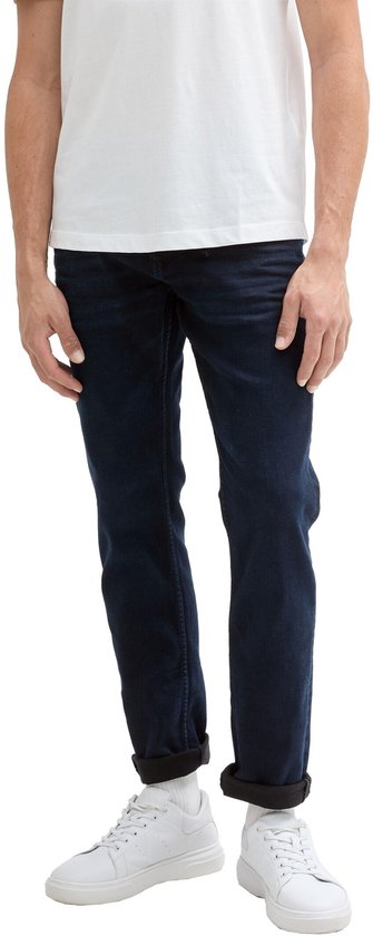 Een man met een witte t-shirt draagt een donkerblauwe slim fit jeans met omgeslagen broekspijpen.