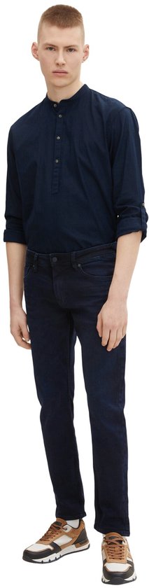 Man in donkerblauwe slim fit jeans en een donkerblauw overhemd met opgerolde mouwen en sta-kraag.