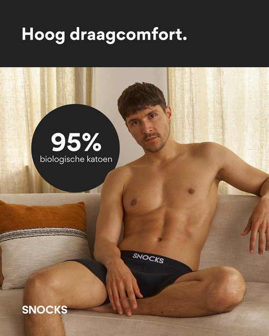 Man zit op een bank, draagt zwarte SNOCKS boxershorts. Cirkel met '95% biologische katoen'.