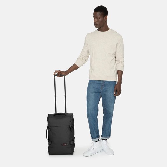 Zwarte koffer met uittrekbare handgreep, getoond naast een man in jeans en een crème sweater.