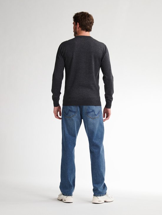 Man staat met zijn rug naar de camera in een donkergrijze gebreide trui en blauwe jeans.