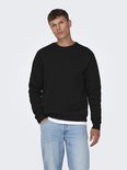 Man met zwarte sweater en spijkerbroek, hand in de zak.