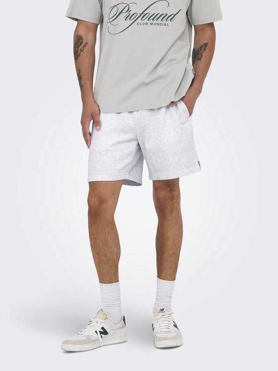 Man met een grijze sweatshort, witte sokken en sneakers. Hij draagt een grijs shirt met tekst.