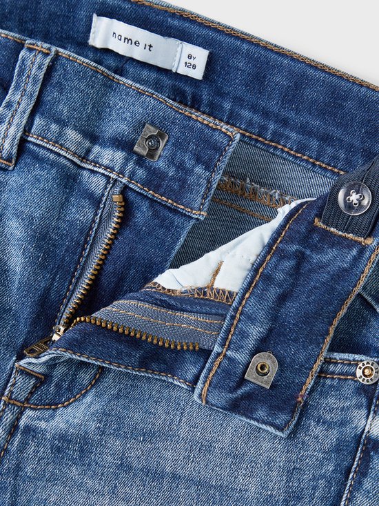Gedetailleerde close-up van de tailleband van een spijkerbroek met knoop, rits en verstelbare elastiek aan de binnenkant.