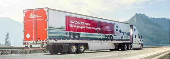 Een witte trailer met een rode reclamebanner en rode en witte reflecterende strepen langs de zijkant.