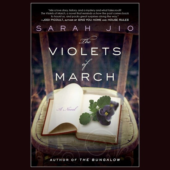 Boek met de titel "The Violets of March" door Sarah Jio, met een open boek en paarse viooltjes op een stoel.