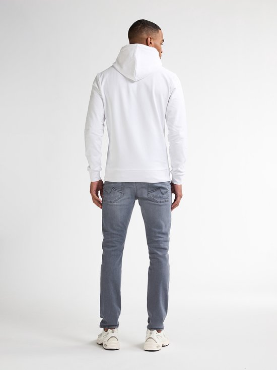 Man van achteren gezien, draagt een witte hoodie en grijze slim fit jeans. Witte sneakers.