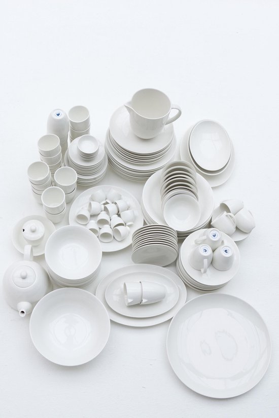 Diverse witte porseleinen serviesstukken, waaronder theepotten, mokken, borden en schalen, verspreid.