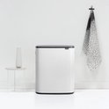 Witte Brabantia Bo Touch Bin prullenbak met donkergrijs deksel, naast een witte vaas op een bijzettafeltje.