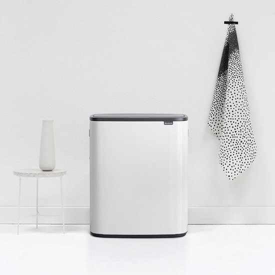 Witte Brabantia Bo Touch Bin prullenbak met donkergrijs deksel, naast een witte vaas op een bijzettafeltje.