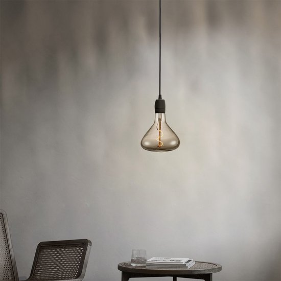 Een rookkleurige LED gloeilamp met spiraalfilament hangt aan een zwarte draad, boven een bijzettafeltje.