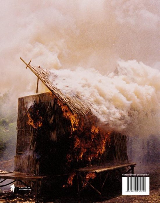 Een hut met een rieten dak staat in brand, omringd door rook.