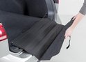 Hand legt zwarte, gevouwen bumperbeschermer in zilveren stationwagen laadruimte.