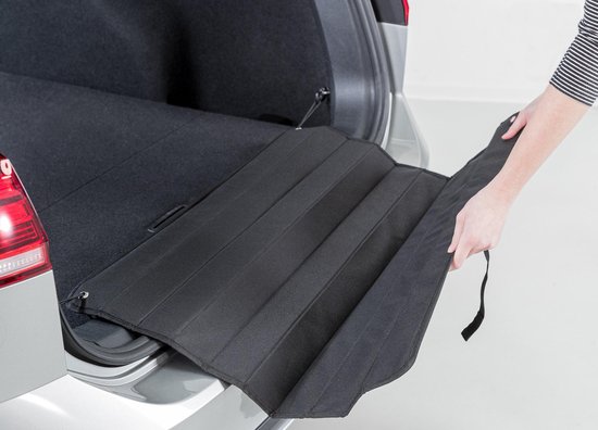 Hand legt zwarte, gevouwen bumperbeschermer in zilveren stationwagen laadruimte.