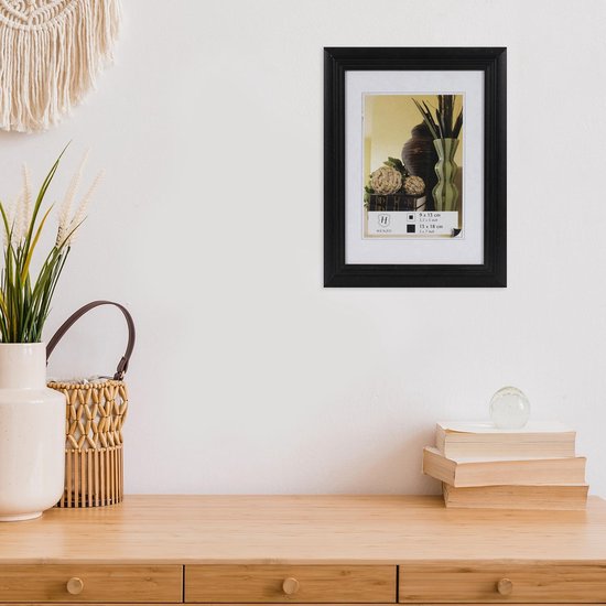 Zwarte fotolijst aan een witte muur boven een houten dressoir.