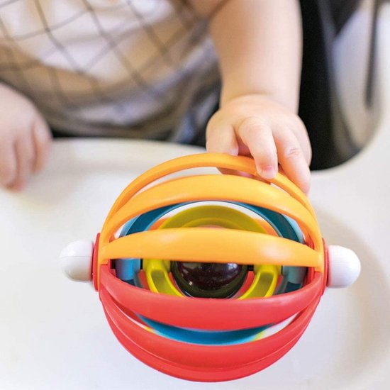Close-up van een baby's hand die een Baby Einstein sticky spinner vasthoudt met rode, oranje, blauwe en gele ringen.