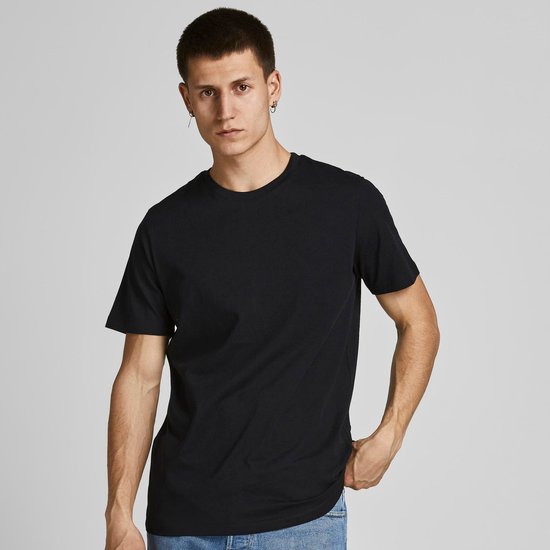 Man met de hand in de zak draagt een zwart T-shirt en een spijkerbroek.