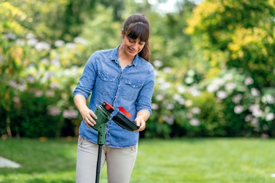 Vrouw demonteert de Bosch grastrimmer in een tuin.