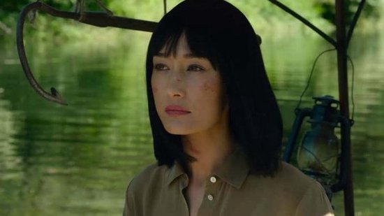 Close-up van Maggie Q met zwart bobkapsel, met schrammen op haar gezicht, bij een meer.