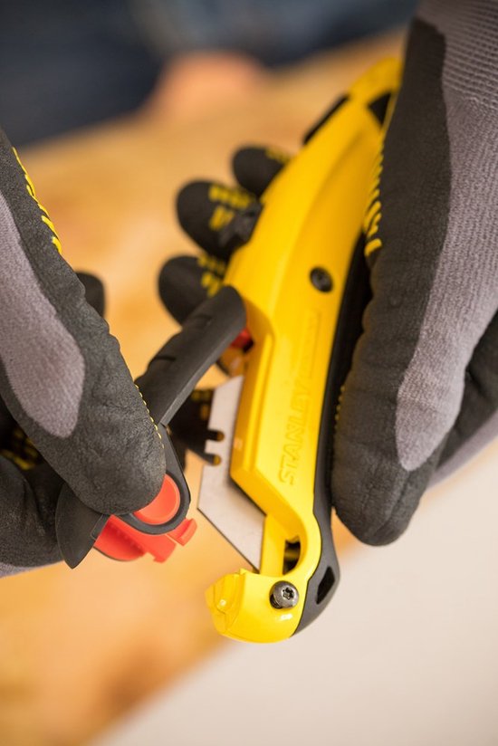 Grijze werkhandschoenen verwisselen een mesje van een geel Stanley Fatmax schuifmes.