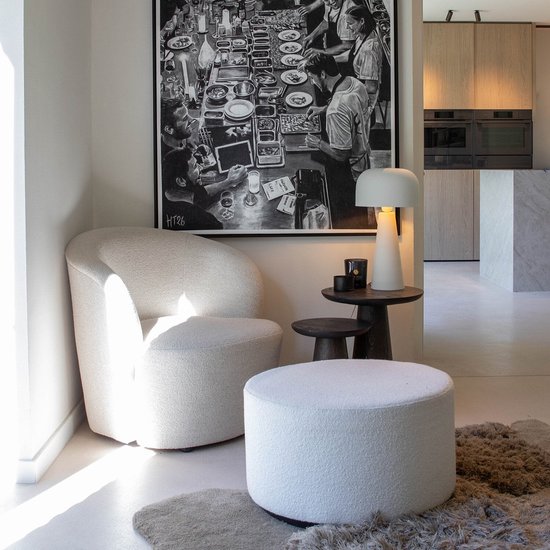 Fauteuil et pouf en bouclé blanc dans un salon ensoleillé avec une grande œuvre d'art noir et blanc.