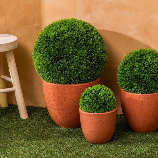 Drie kunstmatige buxusbollen in terracotta potten van verschillende groottes op kunstgras.